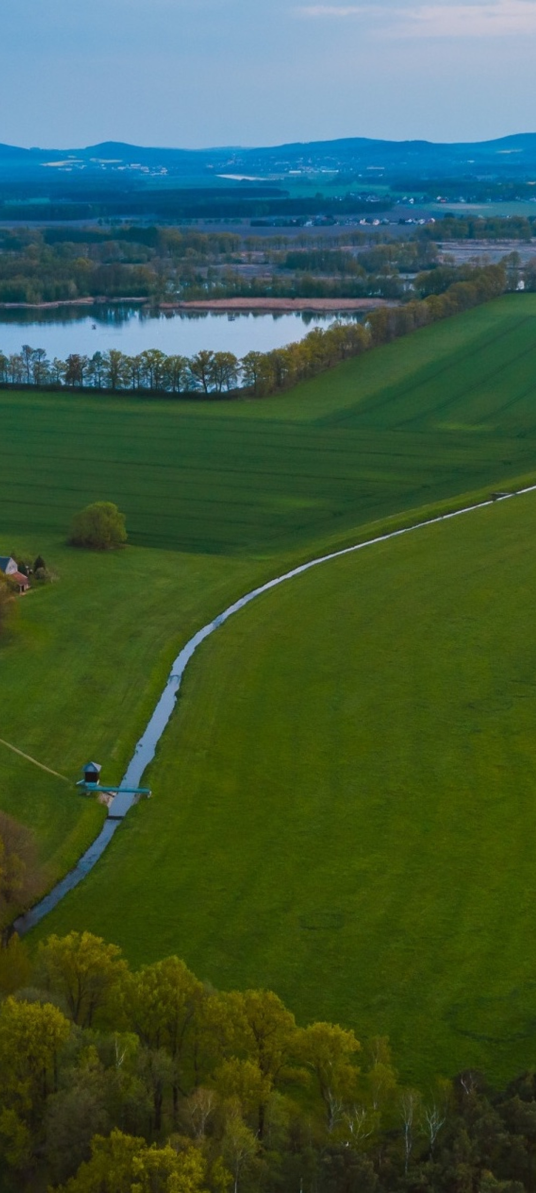 Foto von der Lausitz, grüne Landschaft und ein See, im Hintergrund Berge